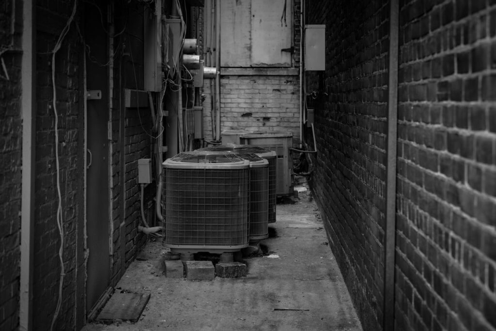 Black and white alley featuring industrial air conditioning units against a brick wall